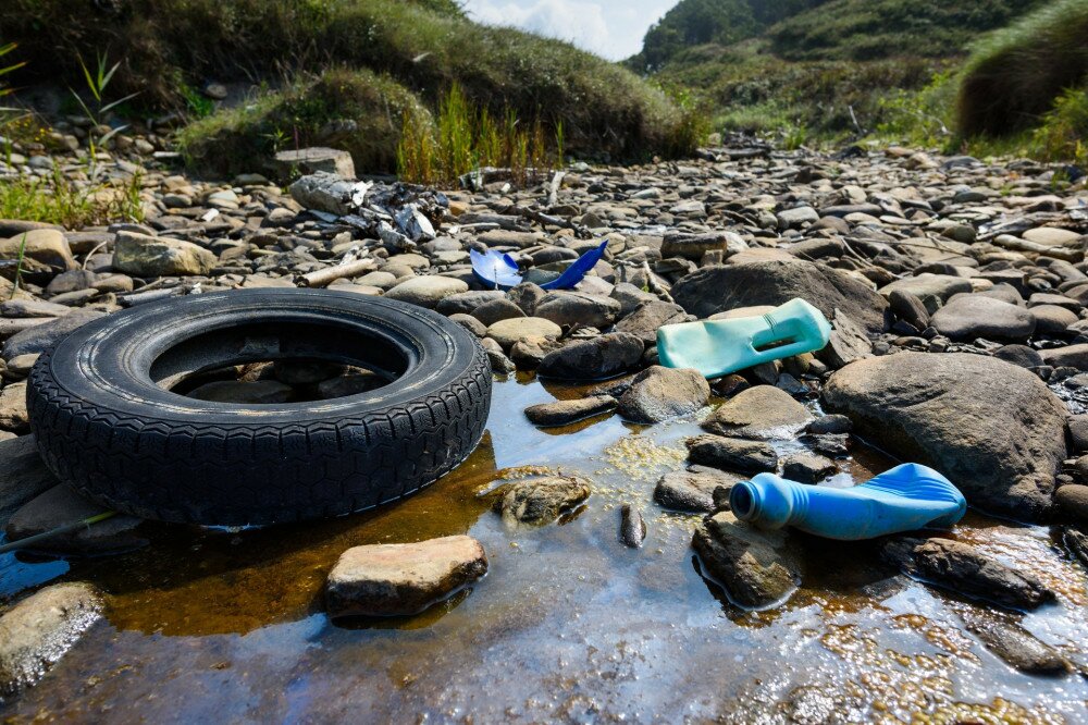 Car tire and plastic bottles in muddy puddle on beach. Beach waste pollution from ocean.