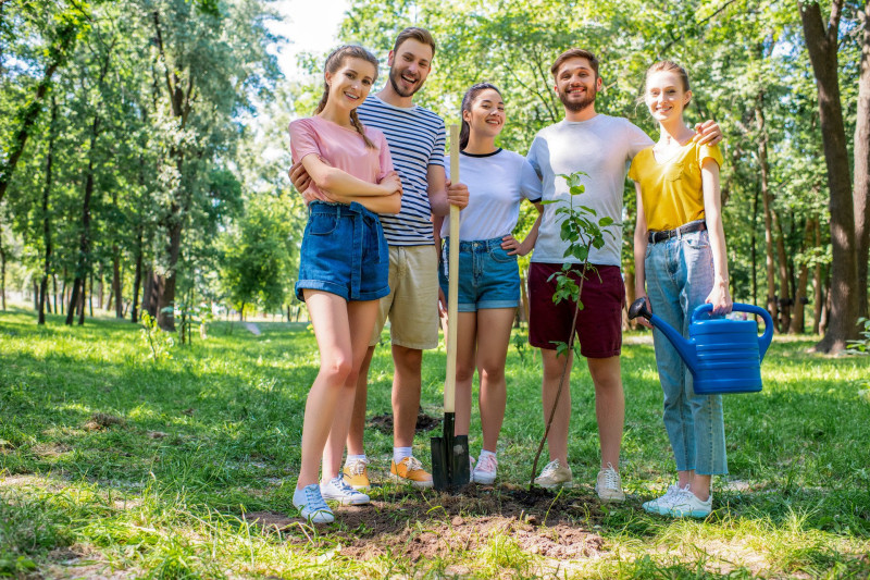 friends with watering can and shovel planting new tree and volunteering in park