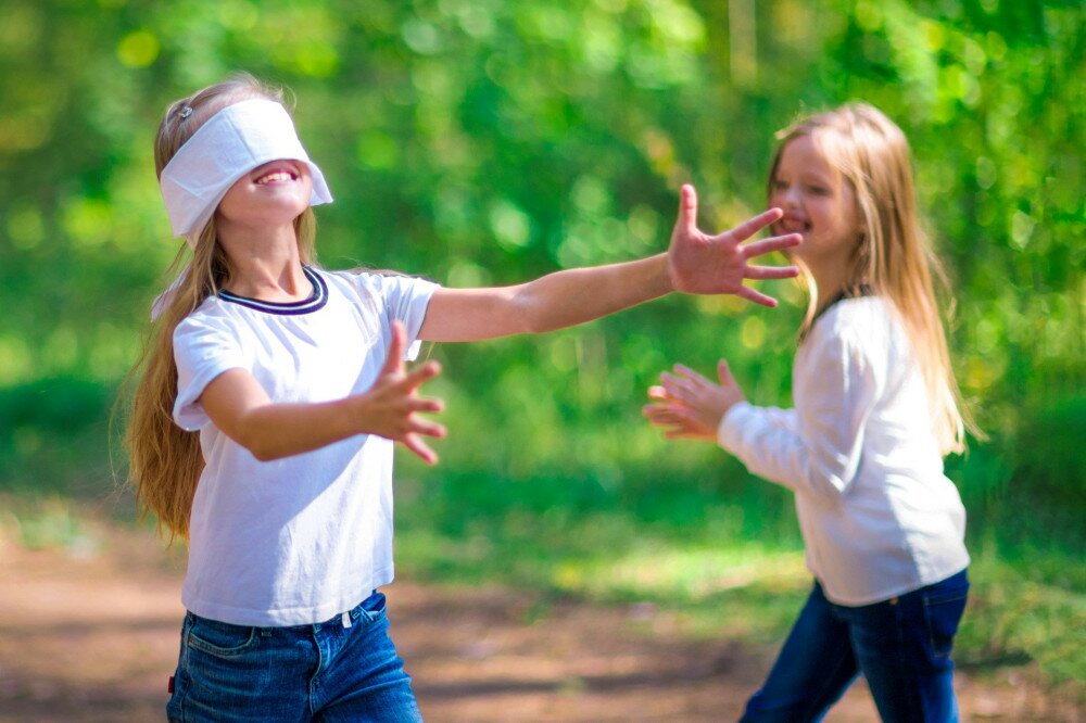 Funny girls play blind man's buff outdoors in the forest.