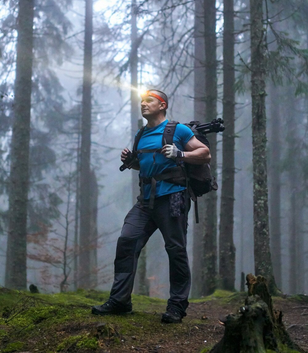 Hiker with headlamp and backpack on a trail in the forest at night