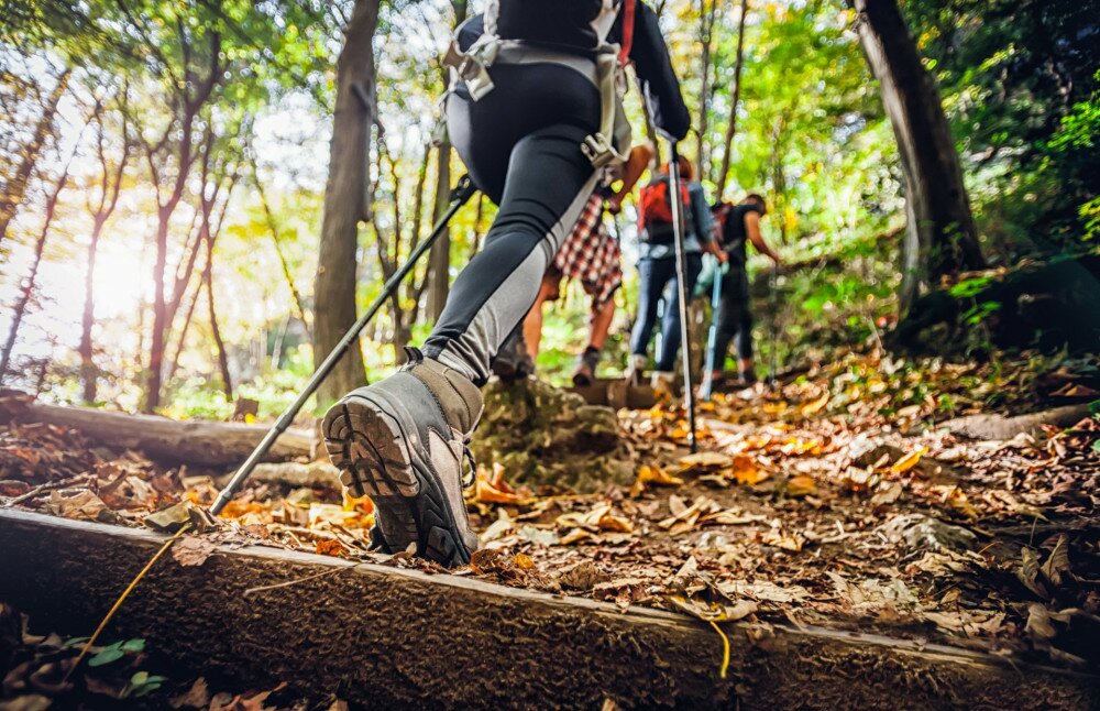 Hiker woman with trekking sticks climbs steep on mountain trail, focus on boot