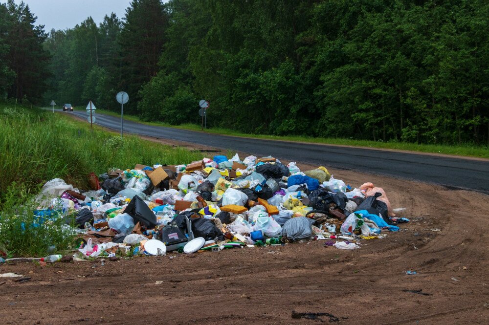 Illegal garbage dump at the intersection of a dirt road and highway. Summer residents go to the city from the village and throw trash along the road