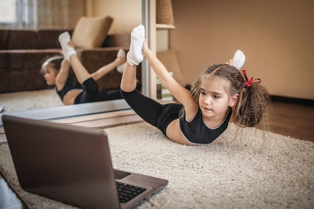 Pretty young girl in sportswear watching online video on laptop and doing fitness exercises at home. Distant training with personal trainer, social distance or self-isolation, online education concept